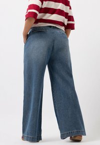 Brede denimbroeken in een middelblauwe wassing, met een hoge taille, achterzakken en rafelige hemden. Afgewerkt met een licht vervaagde textuur.