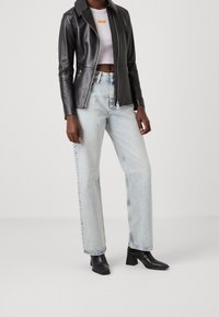 Černá kožená bunda s špičatým límcem, zipovým zapínáním a dvěma předními kapsami, v kombinaci se světle pranými rovnými džíny a černými kotníkovými botami.