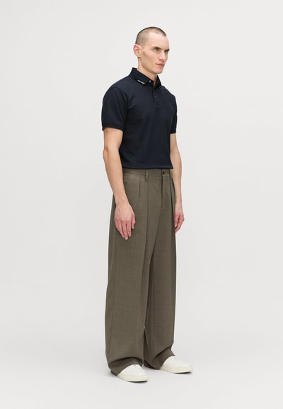 Marinblå polo med kort ärm och märkeskrage, i kombination med beigefärgade vida byxor och vita sneakers. Enkel, modern design.