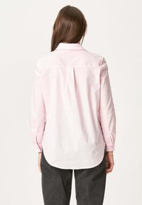 Lys pink langærmet skjorte med svansesøm, rygdetalje og knapmanchetter. Fremstillet af glat stof, med en klassisk krave.