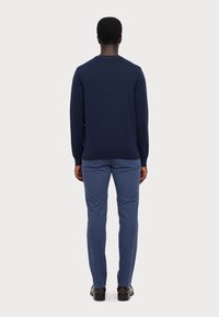 Marinblå stickad tröja med långa ärmar och rund halsringning; kombinerad med ljusblå byxor och svarta skor; sedd bakifrån.