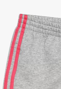 Gray sweatpants featuring a textured fabric, elastic waistband, and prominent pink side stripes. Close-up view highlights detailed stitching.