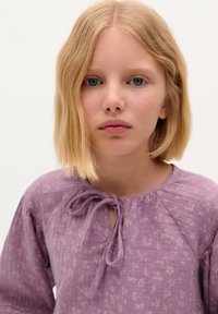 Blusa lilla con un motivo floreale, tessuto testurizzato e scollatura tonda con dettaglio a nodo sul davanti. Le maniche lunghe incorniciano il design.