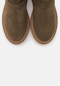 Bottes ankle en daim marron avec une semelle texturée et des coutures autour des bords, dotées d'un design à bout rond.