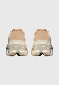 Scarpe da ginnastica in pesca chiaro e crema con tomaia in rete testurizzata, suola bianca spessa e tacco basso, caratterizzate da un design minimale e logo del marchio.