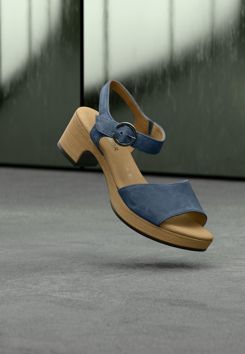 Sandalo con tacco in camoscio blu, punta aperta, cinturino alla caviglia con fibbia circolare e texture in legno sul tacco.