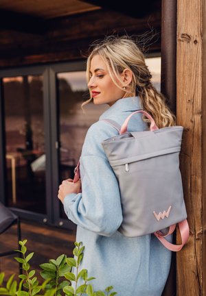 Grauer Roll-Top-Rucksack mit pinken Akzenten, aus glattem Material, mit Logo und verstellbaren Riemen. Wird über einem hellblauen Pullover getragen.