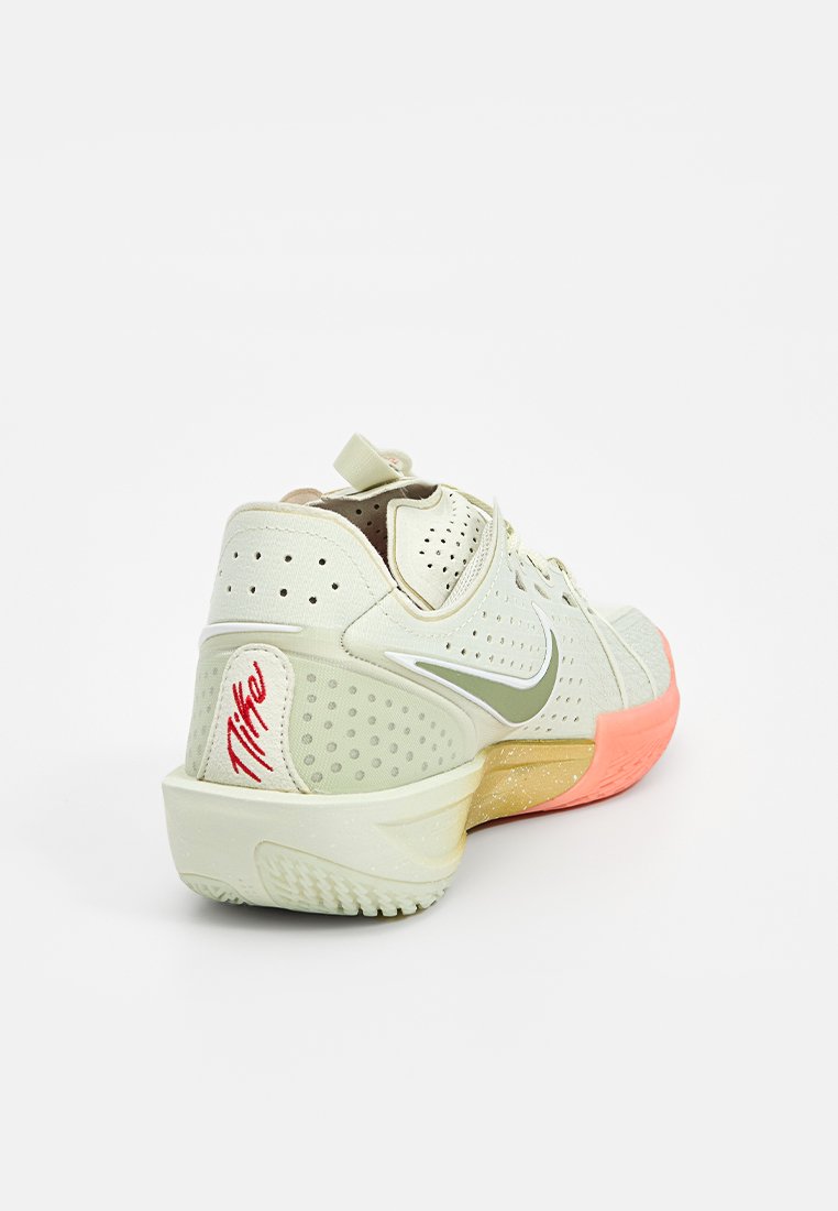 Zapatilla deportiva verde claro con un upper texturizado, perforaciones, un swoosh blanco y una suela degradada de rosa a naranja. Detalle del logo rojo en el talón.