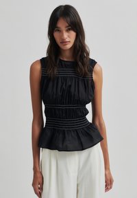 Juodas peplumo tipo topas su susigūdusiu audiniu ir baltais siūlų akcentais. Be rankovių dizainas, lygus tekstūra ir prisitaikanti liemenė.