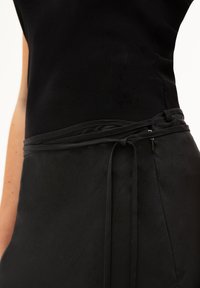 Zwarte top met een ribbelstructuur. Daaronder een gladde zwarte rok met een strik tailleband en een klein ritsdetail aan de zijkant.