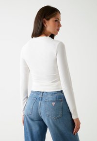 Witte langetermijn top, aansluitend silhouet, zachte stof, gecombineerd met high-waisted blauwe denim jeans met een driehoekig logo patch op de achterkant.