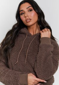 Brun fleece hoodie med en tekstureret, fluffy overflade, snoretræk i hætten og ribbede manchetter. Har en afslappet pasform og blødt stof.