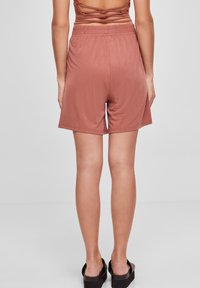 Krátké, vysoké šortky v barvě dusty rose, s elastickým pasem a hladkou texturou, končící těsně nad kolenem.
