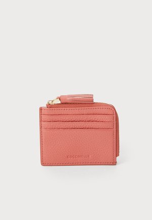 Pink leather cardholder with textured surface, featuring six card slots and a zip compartment, accented with a tassel and gold hardware.