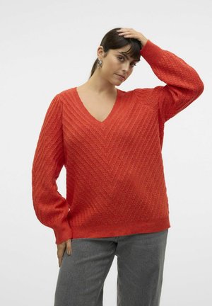 Pull en maille rouge, texturé, avec un col en V et un motif en chevron. Doté de manches longues et larges, avec une coupe décontractée, assorti à un jean gris.