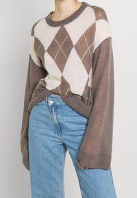 Brun og beige argyle-mønstret sweater med rund halsudskæring, lange ærmer og ribbede manchetter, parret med blå højtaljede jeans.