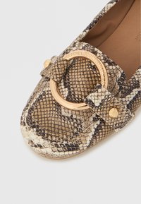 Čevlji z ravnim podplatom v kačjem vzorcu v bež in rjavih tonih, z zlatim okroglim kovinskim dodatkom in teksturirano usnjeno površino.