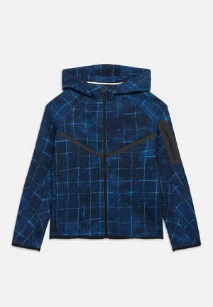 Jachetă albastră cu glugă, cu model în carouri albastre deschise, fermoar frontal complet și buzunar cu fermoar pe mâneca stângă.