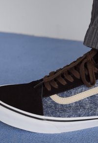 Black suede and denim sneaker with a tan logo stripe, brown laces, white rubber soles, and textured fabric. Mid-top design.