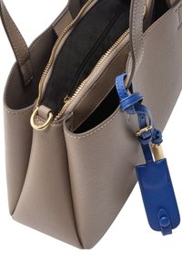 Torebka skórzana w kolorze taupe z złotym zamkiem i niebieskim skórzanym breloczkiem przymocowanym do uchwytu, z widocznymi wieloma przegrodami.