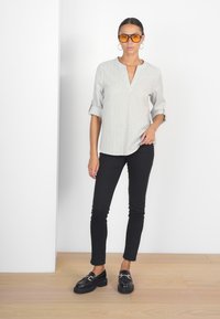 Vit- och svartrandig skjorta med knappar, uppvikta ärmar, kombinerad med svarta slim-fit jeans och kraftiga svarta loafers. Modellen bär orangea solglasögon.