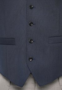 Gilet bleu marine en tissu texturé, doté de six boutons noirs, de deux poches et d'un ourlet en V. Convient pour une tenue formelle.