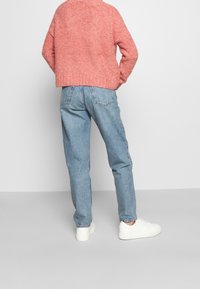 Pull rose texturé, court, associé à un jean bleu clair à jambes droites et des baskets blanches, vu de dos.