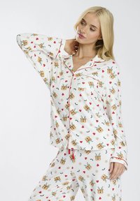 Completo pigiama bianco con accenti rossi, caratterizzato da un motivo di renne, cuori e fiocchi di neve. Tessuto morbido e design morbido.