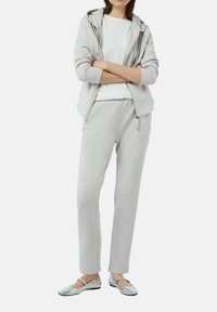 Jasnoszara bluza z kapturem i zamkiem z przodu, zestawiona z dopasowanymi zwężającymi się spodniami dresowymi oraz srebrnymi płaskimi butami. Gładka faktura materiału.