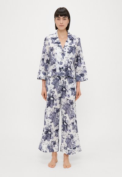 Bloemmotief pyjama set in wit en marineblauw, met een knoopsluiting top met kraag en wijde broek. Zachte stof met een gladde afwerking.