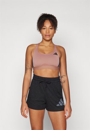 Light pink sports bra with black accents, paired with loose-fitting black shorts featuring a subtle pattern and Adidas logo detail.