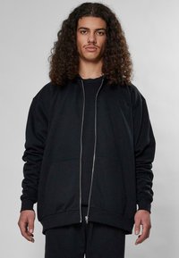 Felpa nera con zip, maniche lunghe, polsini a costine, due tasche frontali e una vestibilità comoda. La trama del tessuto è liscia e morbida.