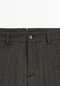 Ciemnoszare wełniane spodnie z zapięciem na guzik, szlufkami na pasek i subtelnym wzorem jodełki widocznym na całej tkaninie.