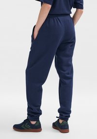 Pantaloni della tuta blu navy con vita elasticizzata e caviglie elastiche, dotati di tasche laterali. Abbinati a sneakers nere e verdi.