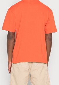 T-shirt arancione a maniche corte con collo rotondo, tessuto di cotone morbido, vestibilità rilassata e senza loghi o motivi visibili. Vista posteriore mostrata.
