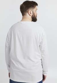 Weißes Langarm-T-Shirt aus Baumwolle mit Rundhalsausschnitt und lässigem Schnitt, kombiniert mit blauen Jeans. Rückansicht gezeigt.