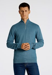 Herrtröja i teal med dragkedja vid kragen, långa ärmar, ribbade cuffs och fåll. Tillverkad i ett mjukt material med en slät yta och figursydd passform.