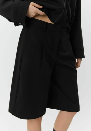 Pantaloni scurți negri plisati cu croială ajustată, confecționați dintr-un material neted. Se disting prin talie cu bucle pentru curea și buzunare laterale.