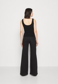 Sort ribbet tanktop med bølget halsudskæring, parret med brede sorte jeans. Bagfra ses det enkle design og pasform.