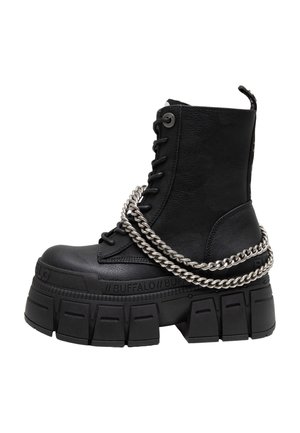 Bota de combate negra de cuero con plataforma, suela gruesa y robusta y cadena plateada envuelta alrededor del tobillo y los cordones.