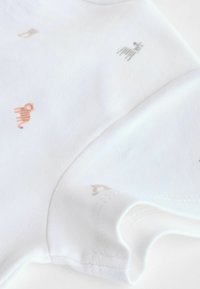 Hvid bomulds t-shirt med korte ærmer, der har diskrete dyreprint i grå og orange. Glat tekstur med en buet halsudskæring og kontrastsyning.