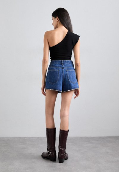 Top nero a costine con una spalla, pantaloni shorts in denim blu scuro a vita alta con dettagli simili a perle e stivali bordeaux al ginocchio con dettagli a taglio.