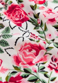 Floral fabric featuring pink and red roses on a white background, with green leaves and black outlines, showcasing soft texture and vibrant colors.