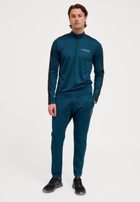 Teal träningstopp med svarta detaljer, halvdragkedja på nacken, tillsammans med matchande teal joggers, som har en smal passform och är tillverkade av lätt och mjukt tyg.