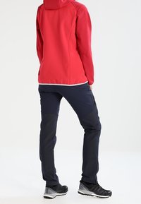 Rød softshelljakke med hætte og kontrastfuldt hvidt foer. Kombineret med marineblå bukser med tekstureret stof og sorte atletiksko.