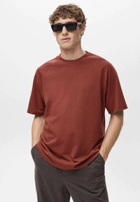 Ruda, krótko rękawowa koszulka T-shirt z okrągłym dekoltem i rękawami raglanowymi, wykonana z gładkiego materiału, w połączeniu z ciemnymi okularami przeciwsłonecznymi.