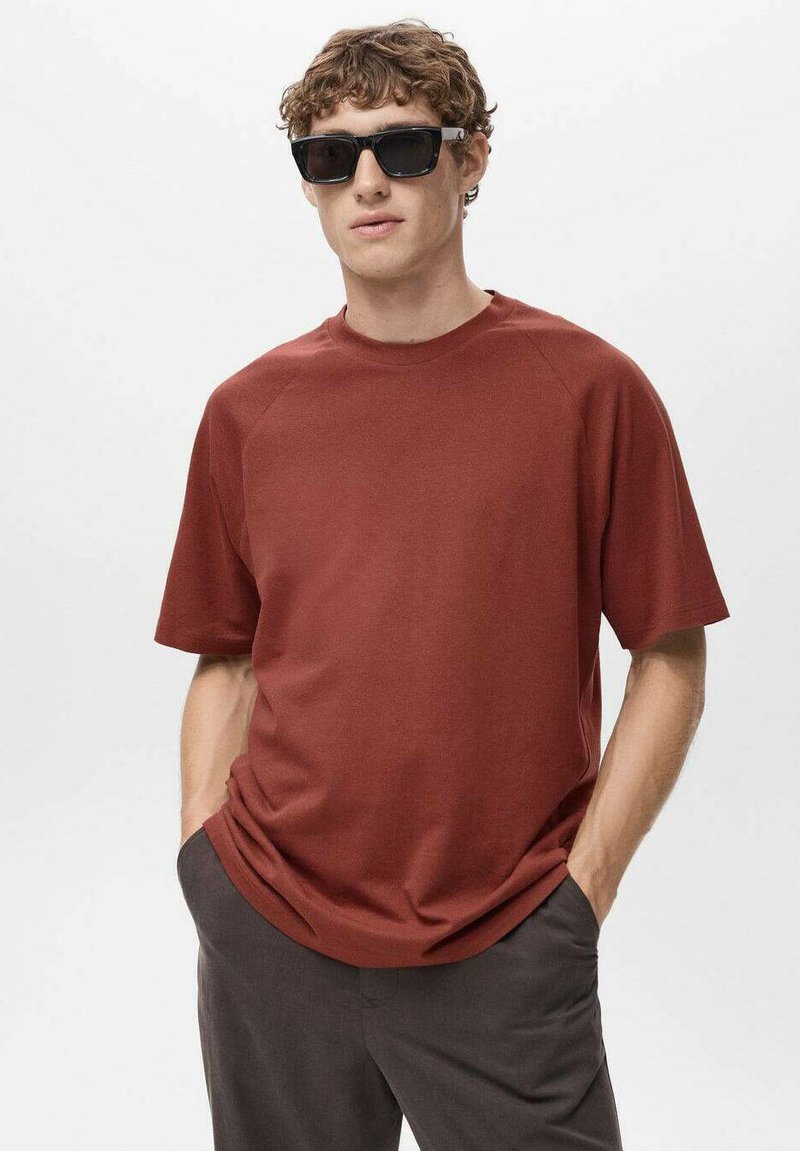 Ruda, krótko rękawowa koszulka T-shirt z okrągłym dekoltem i rękawami raglanowymi, wykonana z gładkiego materiału, w połączeniu z ciemnymi okularami przeciwsłonecznymi.
