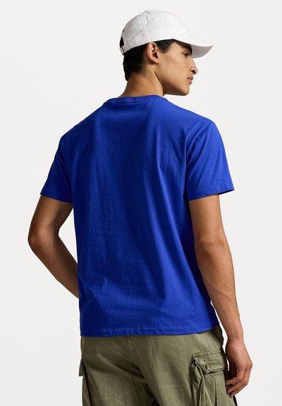 Camiseta de manga corta azul de algodón, con cuello redondo, diseño sencillo y textura suave; llevada con pantalones cargo.