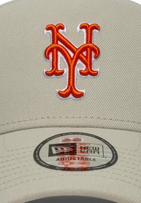 Μπεζ καπέλο μπέιζμπολ με ανάγλυφο πορτοκαλί κεντημένο λογότυπο "NY", διαθέτει υφασμάτινη υφή, ρυθμιζόμενο πίσω μέρος και στρογγυλή ετικέτα με την ένδειξη "New Era Adjustable".