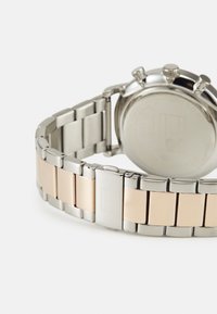 Correa de reloj de acero inoxidable de color plata y oro, con eslabones entrelazados, acabados cepillado y pulido, y un cierre rectangular liso.
